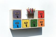 a wooden shelf with colorful drawers and pencils in it on a white wall background