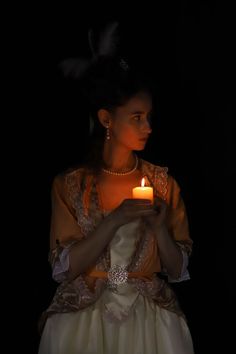 a woman holding a lit candle in her hands and wearing a dress with feathers on it