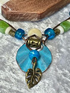 Colorful Turquoise Patina and Bronze charm woven on 1mm Bronze Leather cord with a Bronze Leaf charm and Blue Bone. Mated with bright blue Pony, Peridot color agate, white Bone and Bronze beads come together on two 1mm bronze leather cords with a decorative bronze "S" clasp for closing. Charm is 1" round and total length of necklace is 22". No lead or nickel used. Please use the Last On, First Off approach. Stones discolor with lotions, perfumes, hairspray, sweat, chlorine, even some soaps, and will break if dropped. Bohemian Spacer Beads Necklace For Vacation, Hippie Green Jewelry With Colorful Beads, Nickel Free Multicolor Bohemian Beaded Necklaces, Bohemian Multicolor Nickel-free Beaded Necklaces, Adjustable Nickel Free Green Beaded Necklace, Turquoise Hippie Necklace For Jewelry Making, Hippie Turquoise Necklaces For Jewelry Making, Hippie Turquoise Necklaces, Bohemian Wire Wrapped Jewelry For Vacation