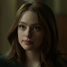 a woman with long brown hair and blue eyes looks at the camera while wearing a necklace