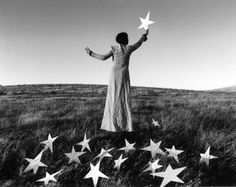 a woman standing on top of a grass covered field holding a star in the air