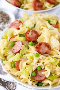 two white bowls filled with pasta, peas and pepperoni on top of a table