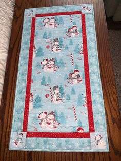 a quilted christmas table runner with snowmen and santa hats on the top, along with candy canes