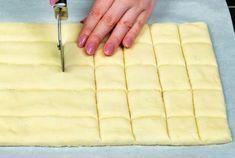 a person using a knife to cut out squares of dough on a sheet of paper