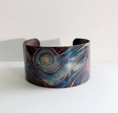 "This unique copper bracelet is made by painting patterns onto copper with a torch, and as the copper heats and cools it turns different colors naturally! Its quite an amazing process! Ive then engraved high lights into the pattern which makes it pop! Such a fun and whimsical design! The cuff is 1\" wide and is flexible enough so that you can make it fit your wrist. It is protected with a sealant to keep it from further oxidizing. These are custom made per order, so please keep in mind that with Copper Cuff Bracelet Wearable Art Gift, Artisan Copper Cuff Bangle Bracelet, Artisan Copper Bangle Cuff Bracelet, Bohemian Electroformed Cuff Bracelet Bangle, Handmade Unique Copper Bangle, Unique Handmade Copper Bangle, Artisan Bronze Copper Cuff Bracelet, Handmade Artistic Copper Bracelets, Wearable Art Copper Bangle Bracelets