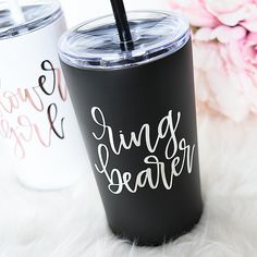 two black and white tumblers sitting on top of a fur covered floor next to pink flowers