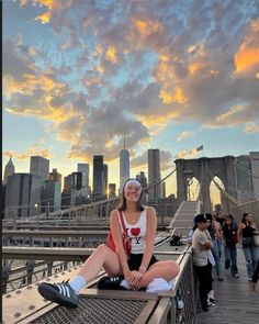 a woman sitting on the edge of a bridge in front of a cityscape