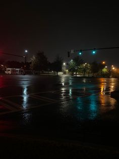 an intersection at night with traffic lights and rain on the ground in the foreground