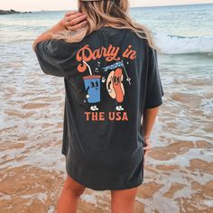 a woman standing on the beach wearing a party in the usa t - shirt and shorts