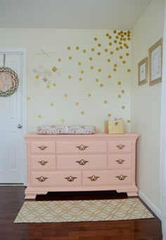 a pink dresser with gold polka dots on the wall in a baby's room