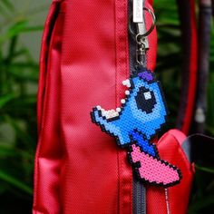 a red backpack with a blue and pink pixelo keychain hanging from it's front pocket