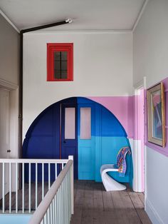 a room with a blue and pink door, white railings and a chair in front of it