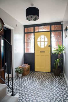 a yellow door in a black and white tiled entryway with potted plants on the floor