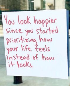 a sign posted on a pole in front of a store window that says, you look happier since you started praizing how your life feels instead of how it looks