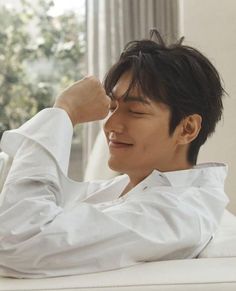 a young man sitting on top of a white couch next to a window holding his arm up