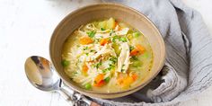 a bowl of chicken noodle soup on top of a gray towel next to a spoon