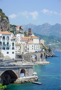 an old bridge over the water with buildings in the back ground and mountains in the background