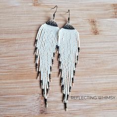 two white and black beaded earrings with fringes hanging from them on a wooden surface