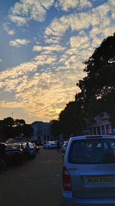 cars are parked on the street as the sun sets in the sky over some buildings