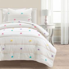 a bed with white sheets and colorful polka dots on the comforter, next to a night stand