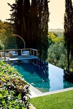 an outdoor pool surrounded by greenery and trees with lounge chairs on the side,