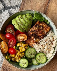 a bowl filled with rice, vegetables and meat on top of a wooden table next to a fork