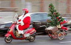 a man dressed as santa claus riding a scooter with a christmas tree on the back