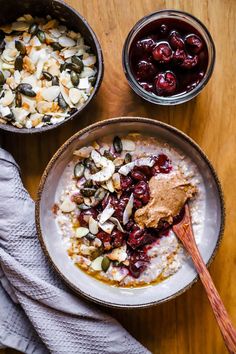 two bowls filled with oatmeal, fruit and nuts on top of a wooden table