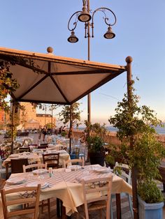 an outdoor dining area with tables and umbrellas over looking the ocean at sunset or sunrise