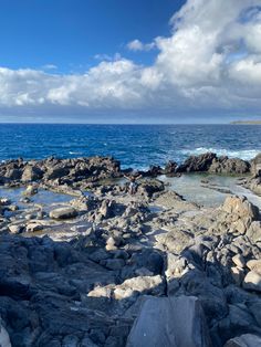 people are standing on rocks near the ocean with blue skies and white clouds in the background