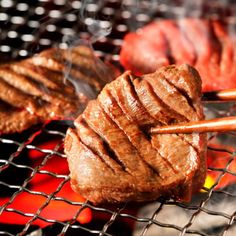 steaks being cooked on the grill with chopsticks