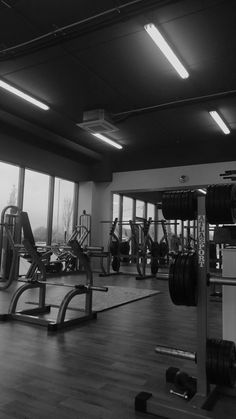 an empty gym with lots of machines and weight plates on the floor in front of large windows