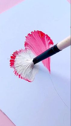 a pink and white flower is being painted on a piece of paper with a brush