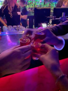 two people are holding up their glasses at a bar while another person sits in the background