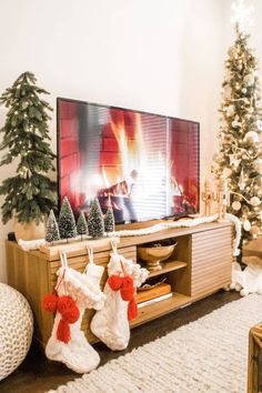 christmas stockings hanging from the legs of a tv stand in front of a fireplace and decorated christmas trees