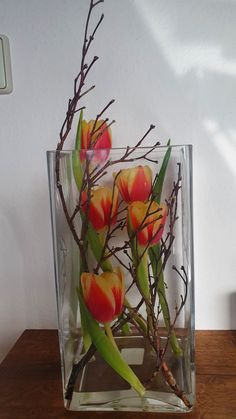 a vase filled with red and yellow flowers on top of a wooden table next to a white wall