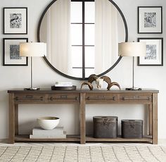 a large round mirror hanging on the wall above a wooden table with drawers and lamps