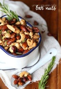 a bowl filled with nuts sitting on top of a table next to rosemary sprigs