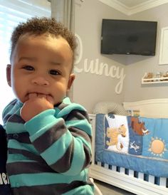 a little boy that is sitting in a crib with his hands on his chin