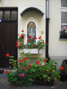 flowers and plants in front of a building with a statue on the window sill