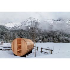 a wooden sauna in the snow with mountains in the background