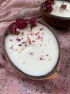 two candles with flowers in them on a pink table cloth next to some brown bowls