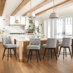 a kitchen with wooden floors and white walls, along with bar stools that are upholstered in grey fabric