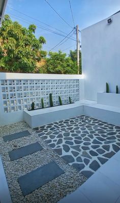 an outdoor area with white walls and grey stones on the ground, surrounded by greenery