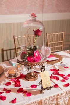 a table topped with a glass dome covered in pink flowers and petals on top of it