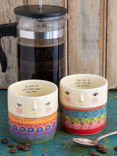 two coffee mugs sitting on top of a table next to a cup with a spoon