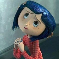 a doll with blue hair is standing in front of a wall and looking at the camera