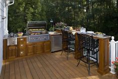 an outdoor kitchen with bar stools and grill on the back deck, surrounded by greenery