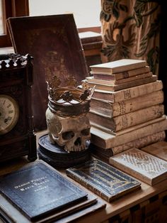 a table topped with lots of books and a skull statue next to an old clock