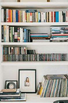 a white bookshelf filled with lots of different types of records and cds on top of it